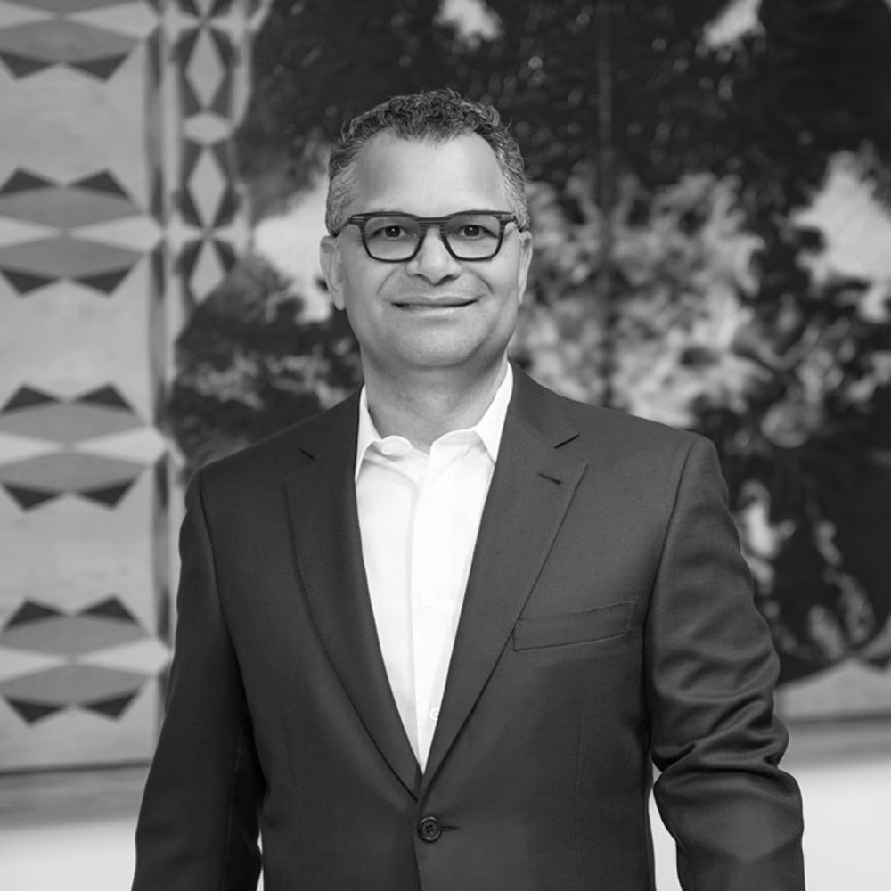 Un hombre con traje y gafas sonríe en una foto en blanco y negro.