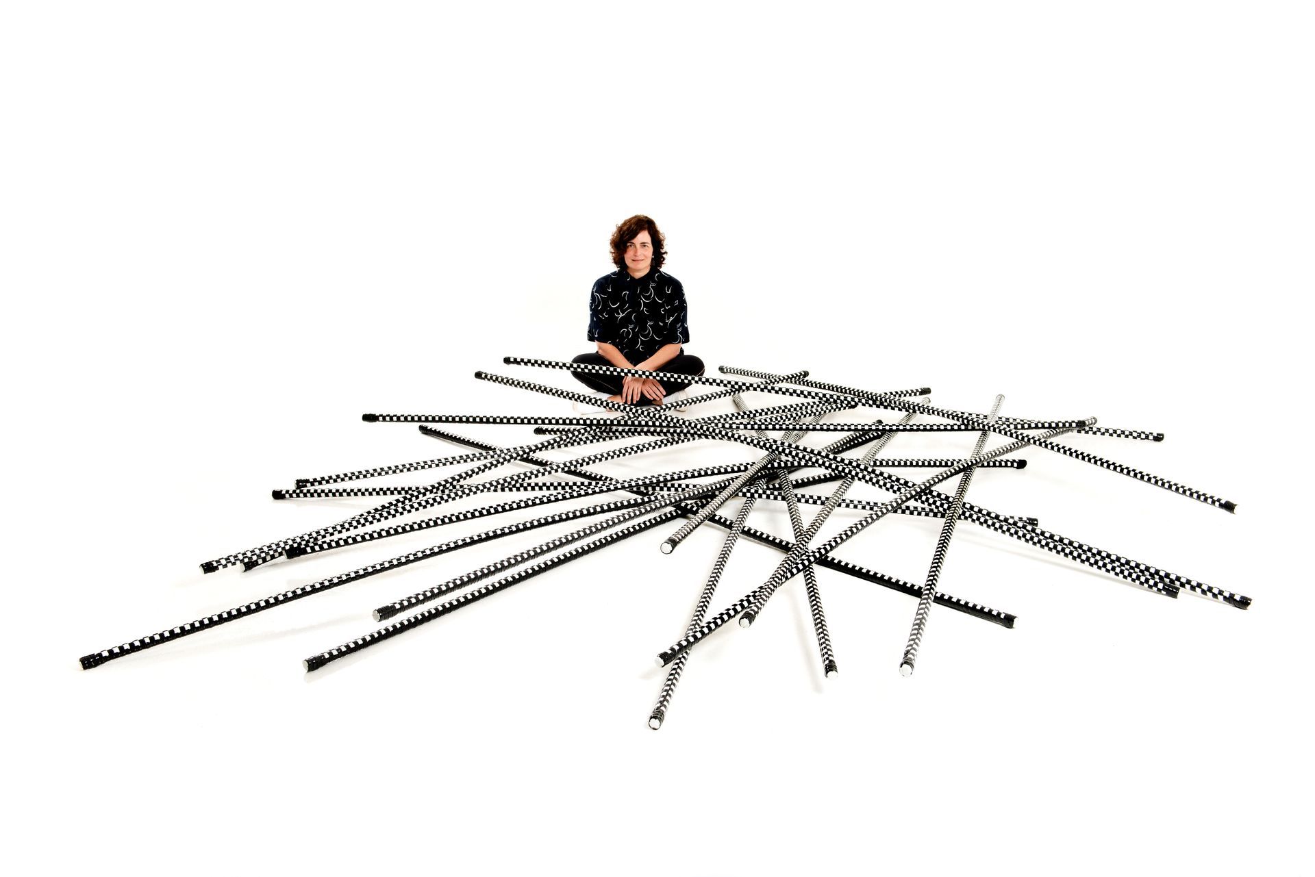 Una mujer se sienta encima de una red de líneas blancas y negras sobre un fondo blanco.