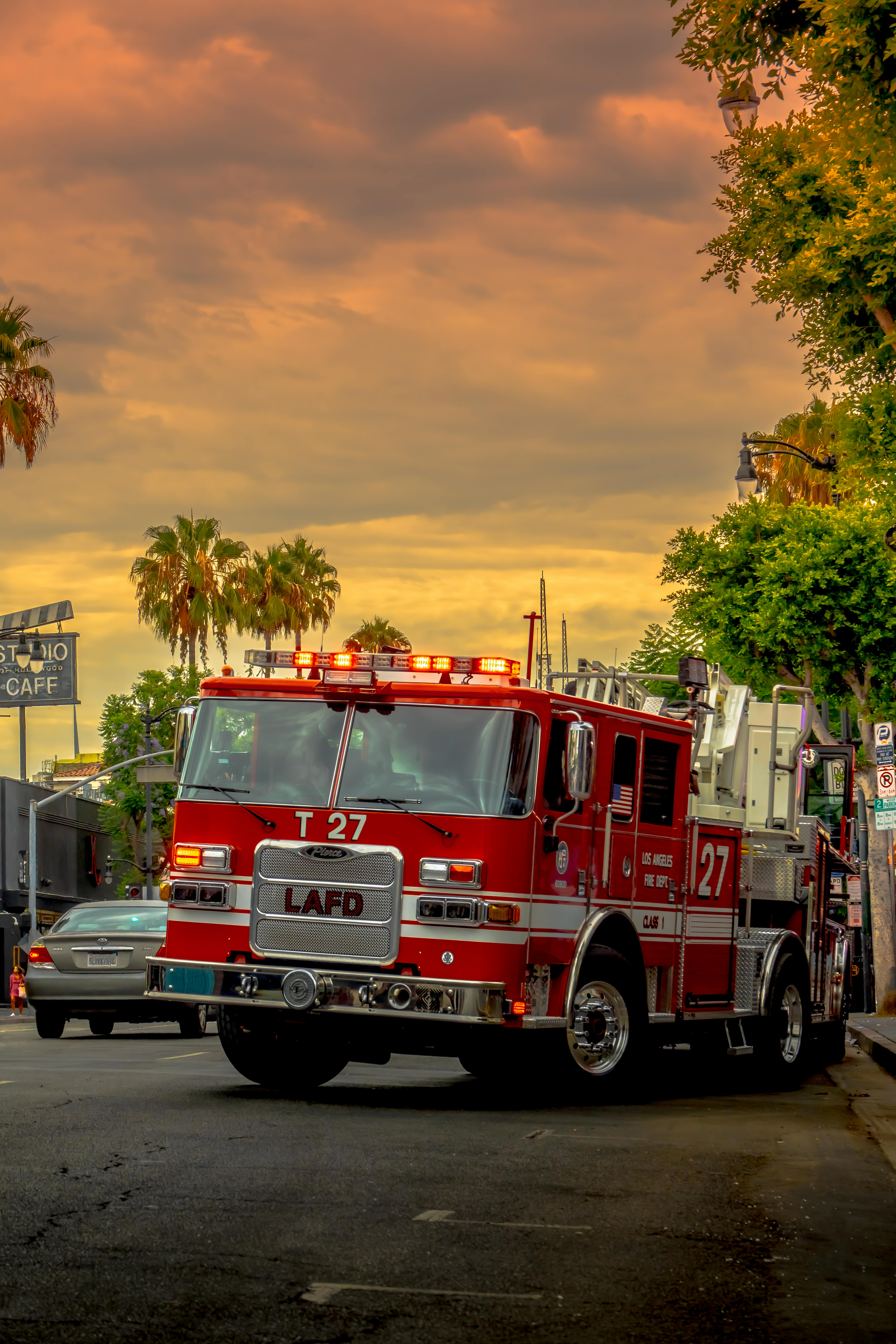 Fire truck, LAFD Engine 27, parked on street. Palm trees and cloudy sky in background.