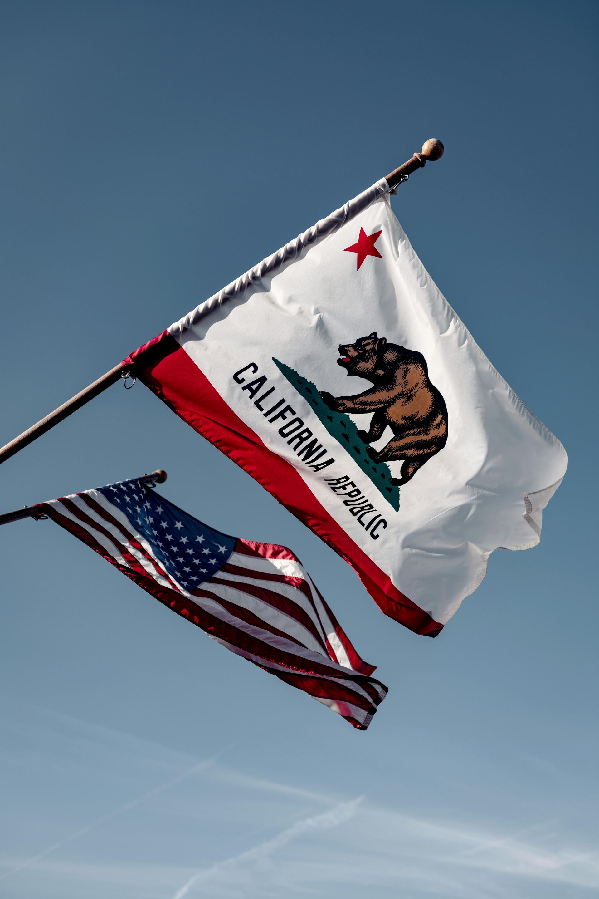 California state flag and American flag waving against a blue sky.