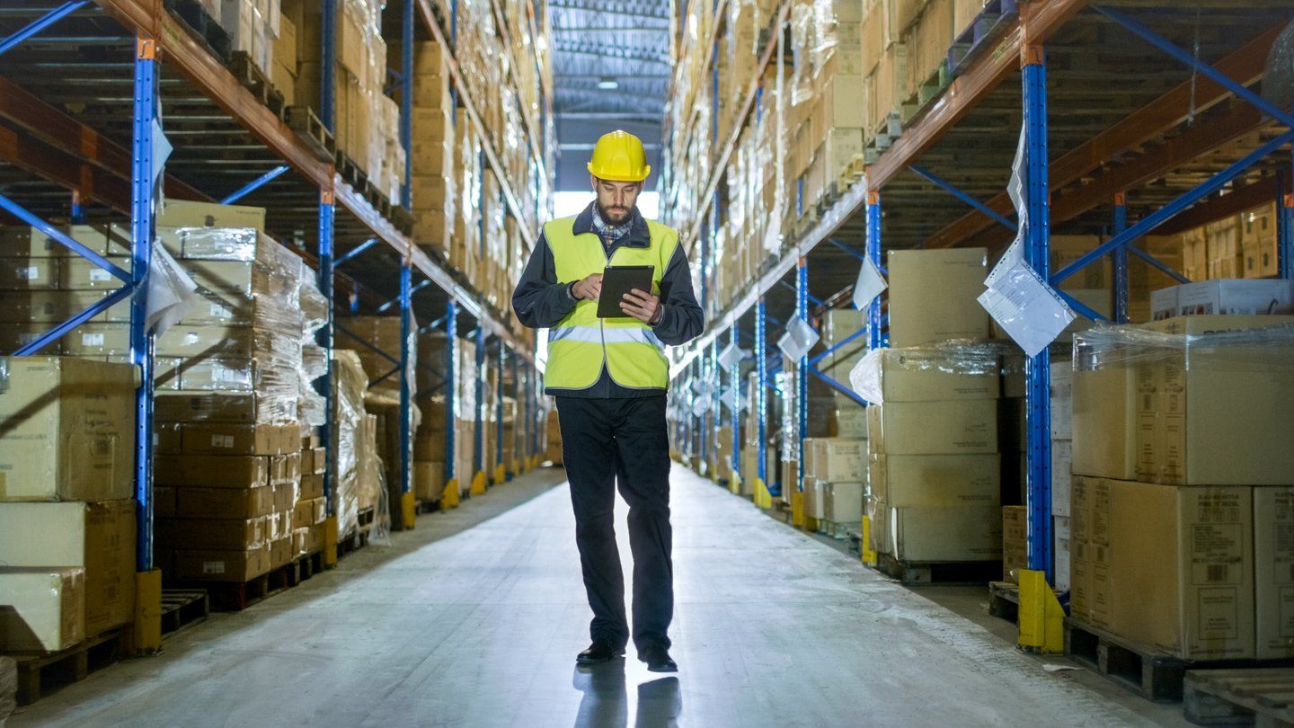 Warehouse worker in yellow hard hat and safety vest standing in a stocked warehouse aisle