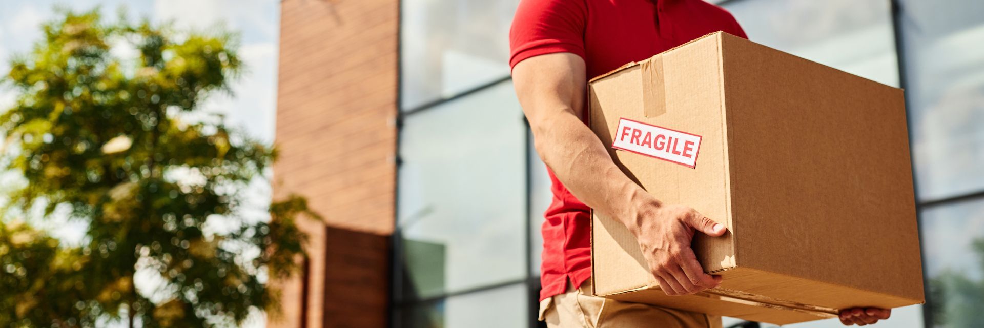 Un fattorino con una maglietta rossa trasporta una scatola di cartone con l'etichetta