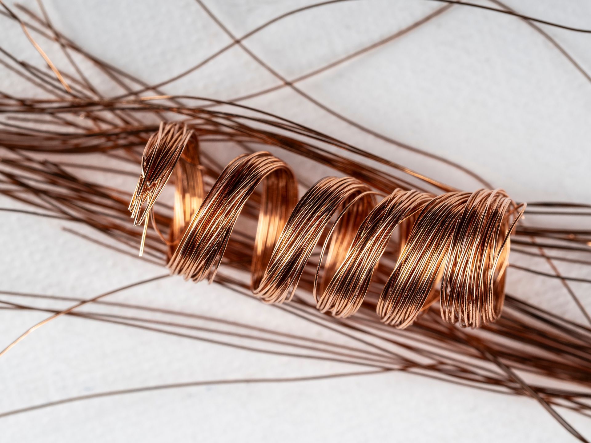 Filo di rame arrotolato, a spirale e disposto su sottili fili marroni, contro una superficie bianca.