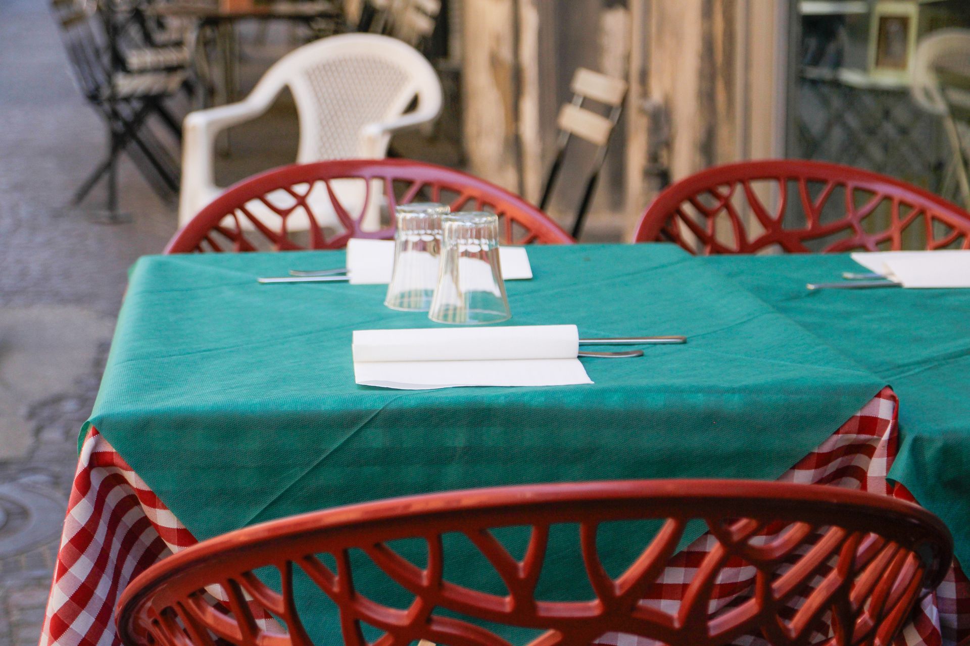 Tavolo da ristorante all'aperto con sedie rosse, tovaglia verde e gonna a righe.