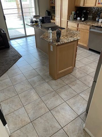 Kitchen with a granite countertop island, light wood cabinets, tile floor, and sliding glass door.