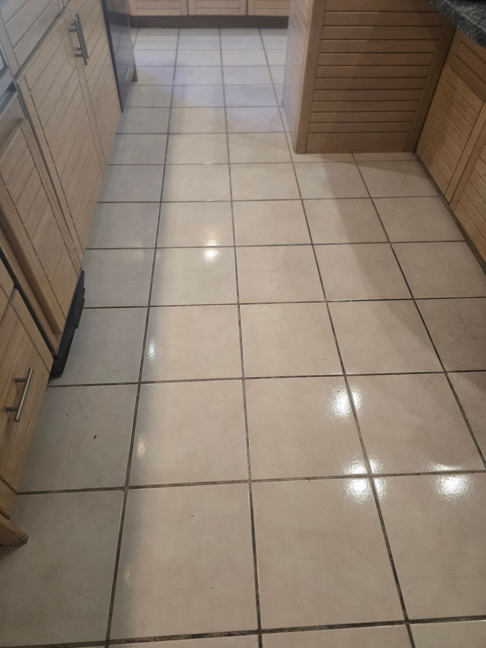 Beige tiled kitchen floor between wooden cabinets.