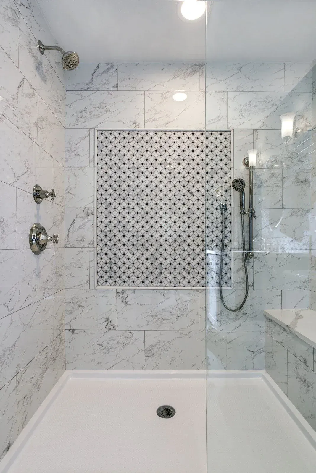 A walk in shower with marble tiles and a glass door.