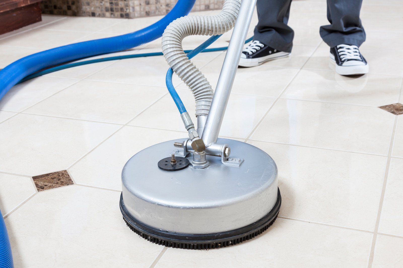 A person is cleaning a tile floor with a vacuum cleaner.