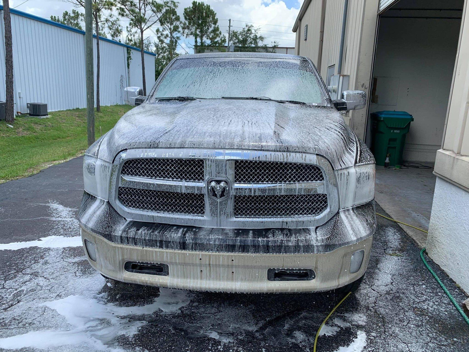 A tan Dodge Ram pickup truck covered in soapy foam, outdoors near a building.