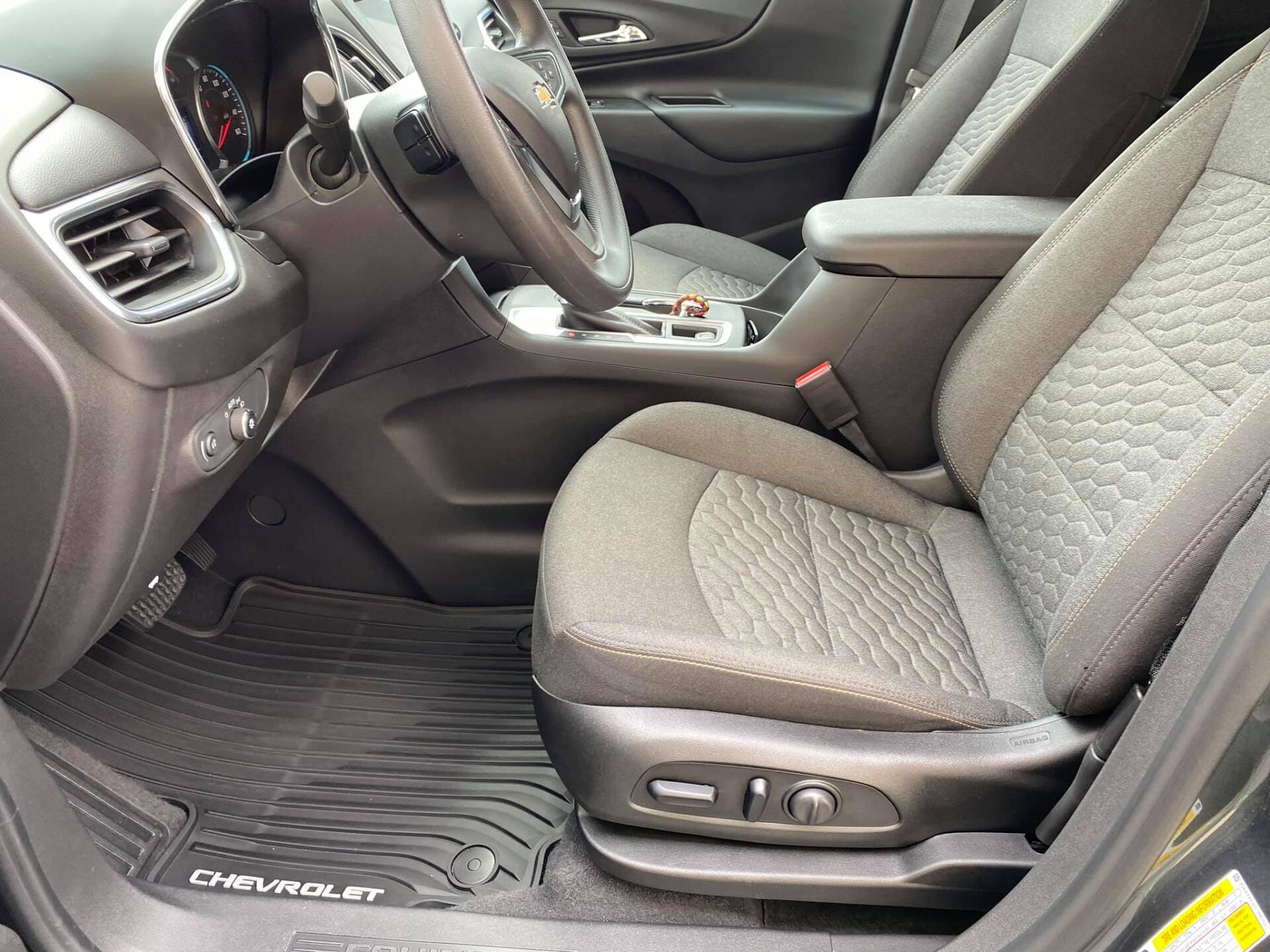 Interior of a Chevy Equinox: black seats, steering wheel, dashboard. Front seat, floor mats.