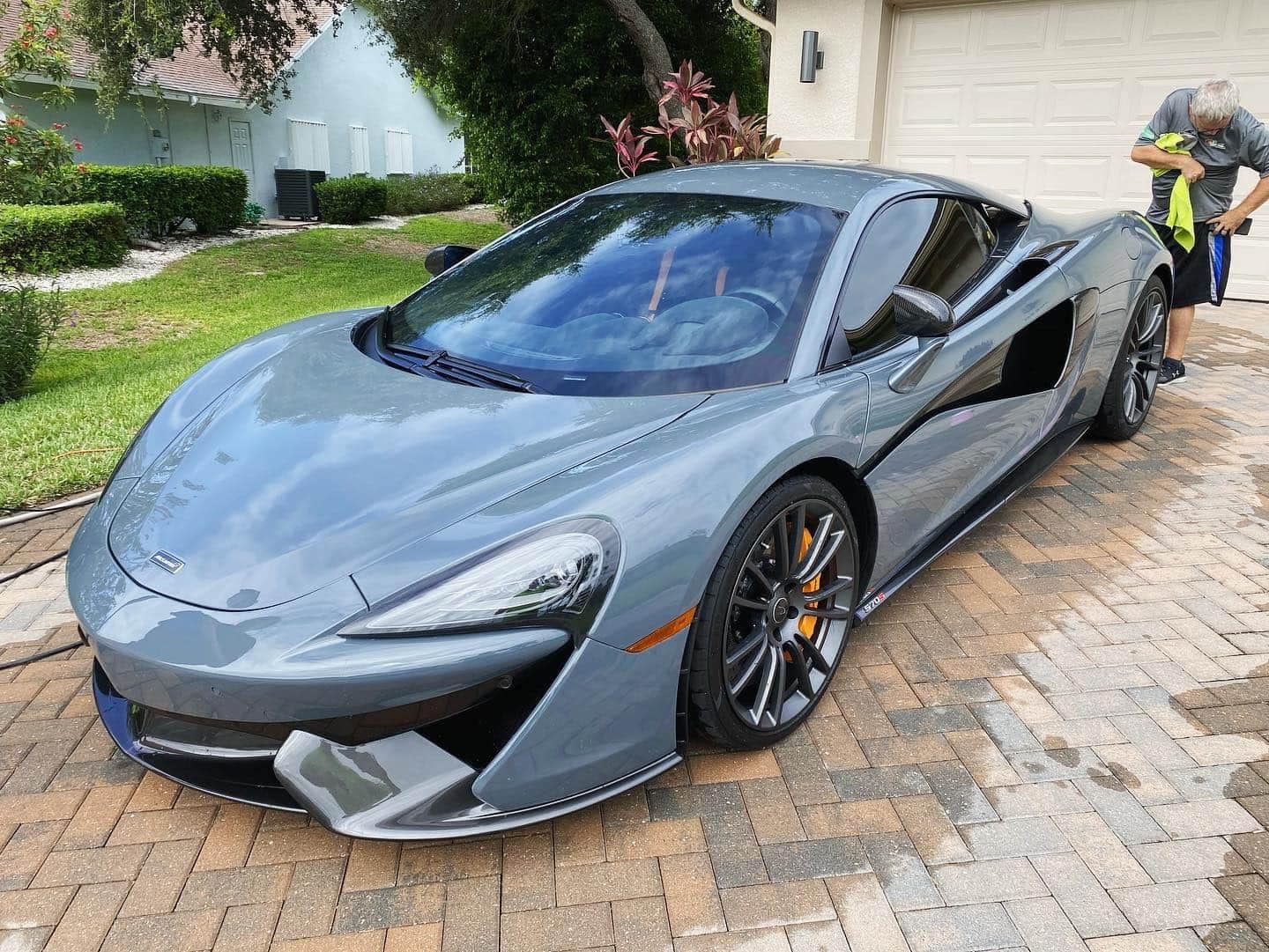 Gray McLaren sports car being detailed in a driveway; person drying the car.