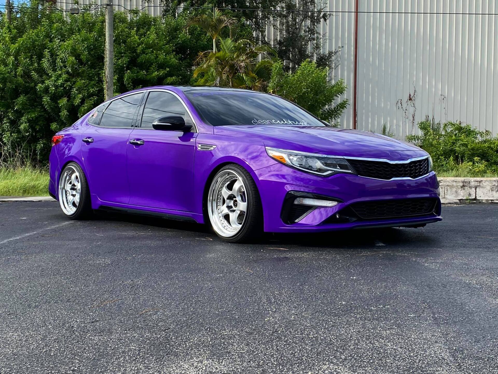 Purple Kia sedan with lowered suspension and chrome wheels, parked in a lot.