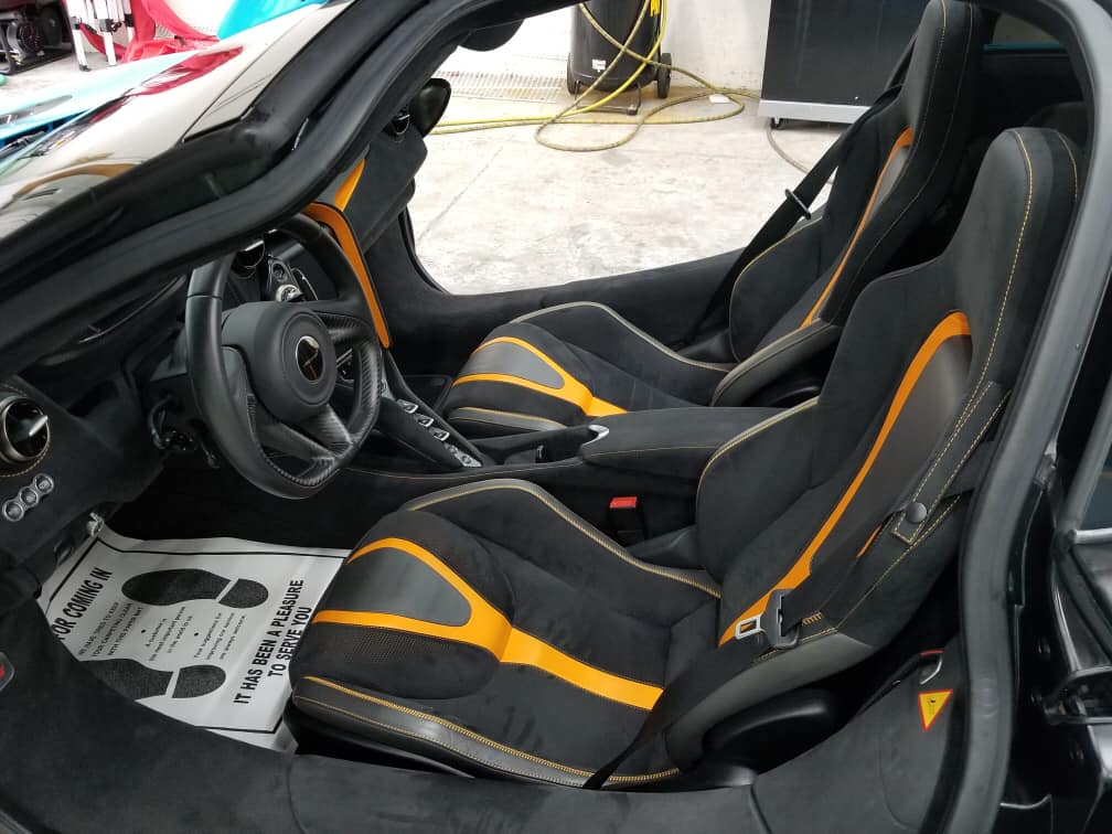 Interior of a black McLaren with orange accents on the seats. Driver's side door open.