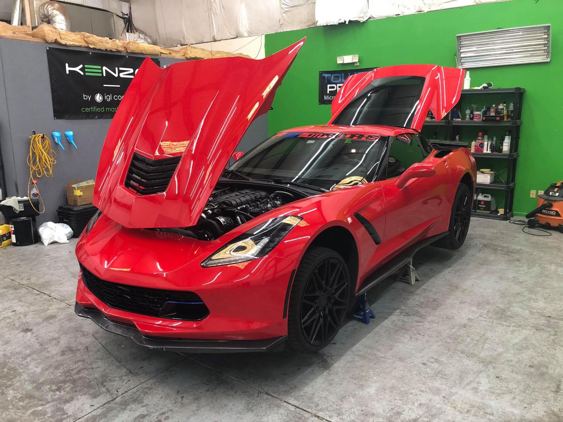Red Corvette with open hood and rear hatch in a garage.