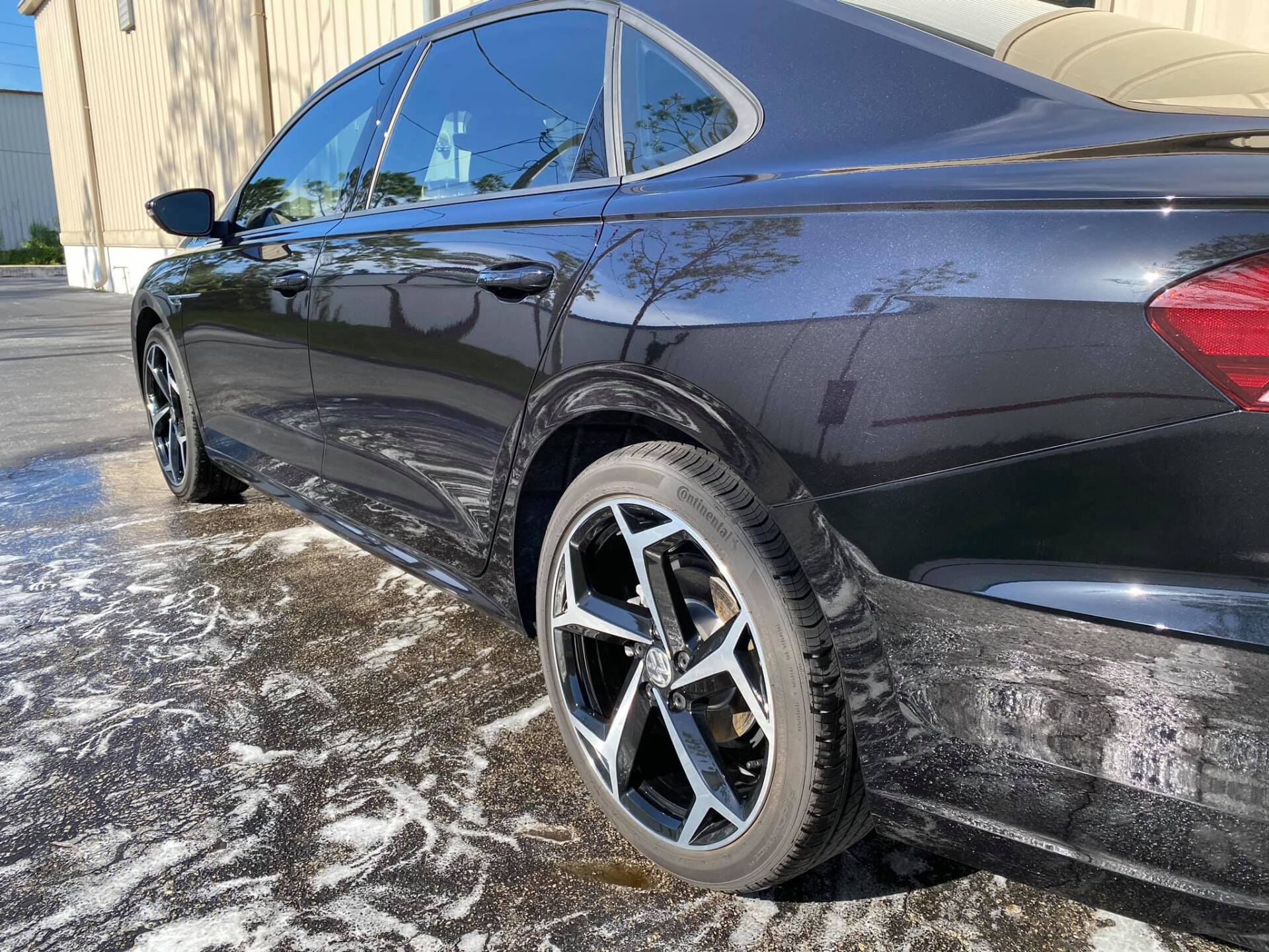 Black sedan being washed with soapy water on a paved surface.
