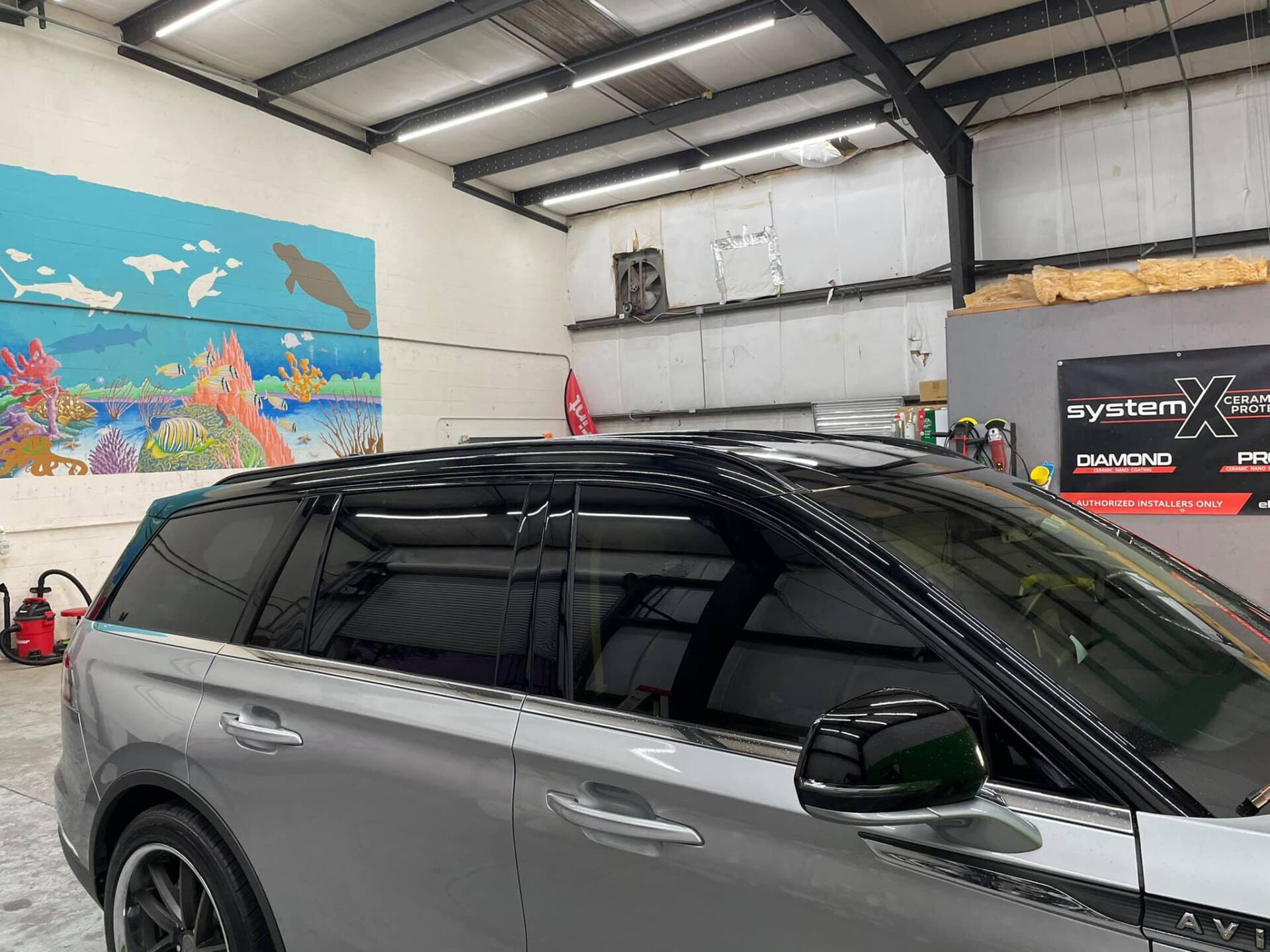 Gray SUV in a garage; tinted windows, black roof, artwork on wall.