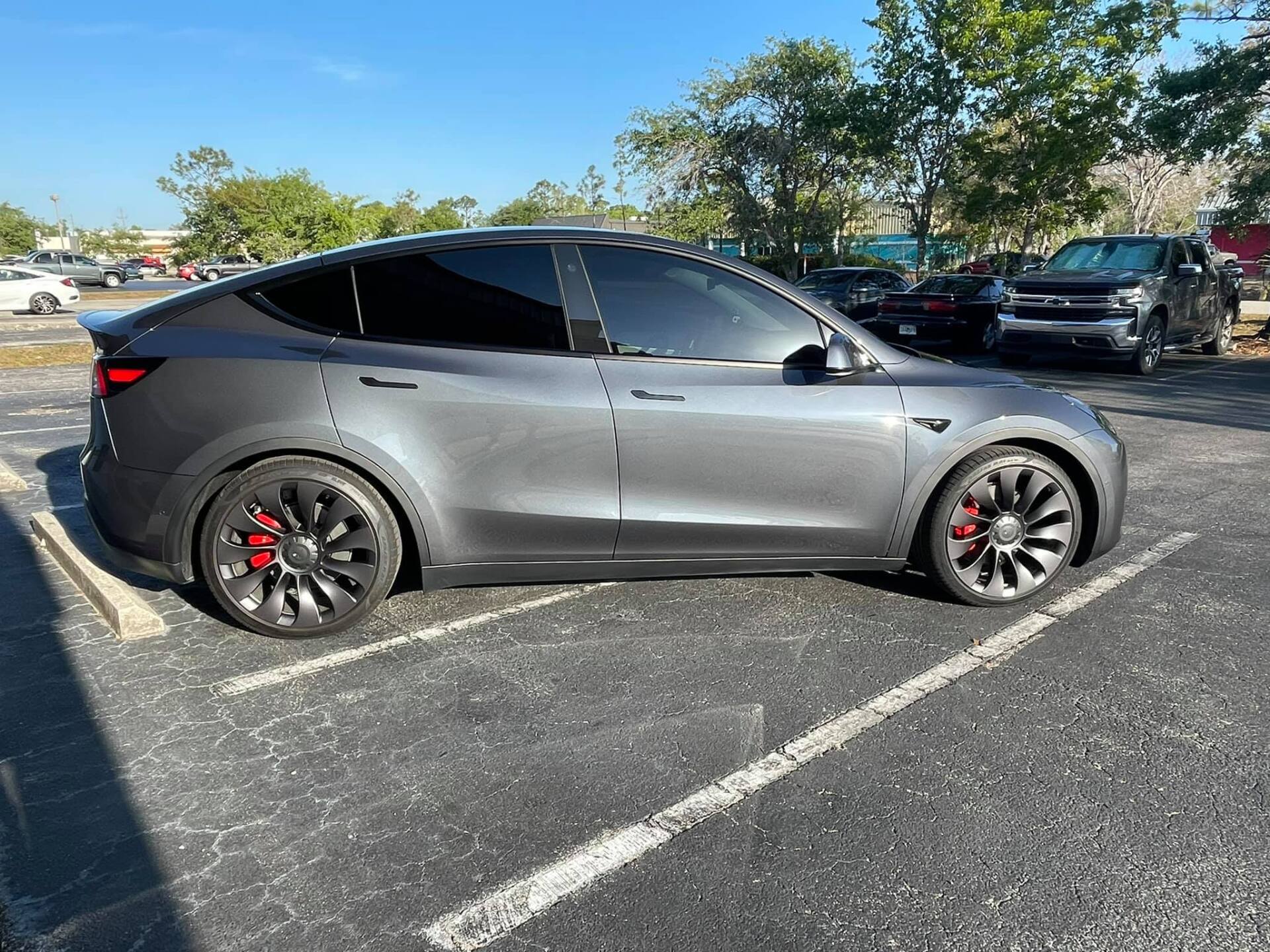 Gray Tesla Model Y with tinted windows and red brake calipers parked in a parking lot.