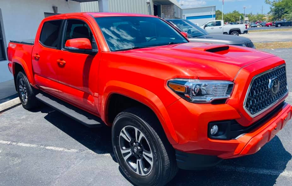 Bright red Toyota Tacoma truck parked in front of a building.