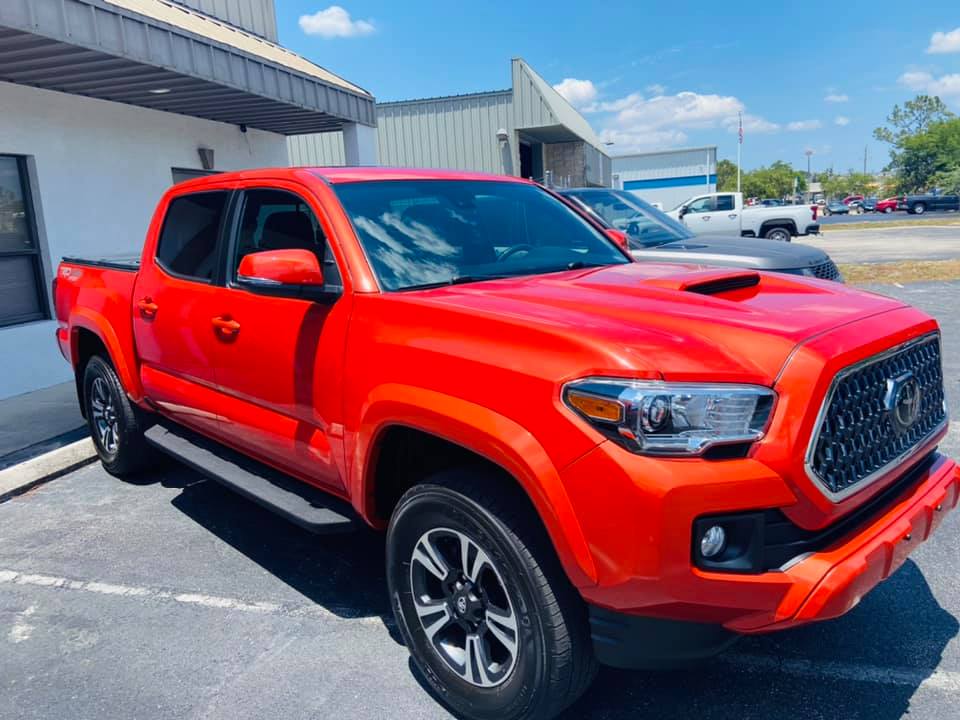 Red Toyota Tacoma pickup truck parked outside, sunny day.