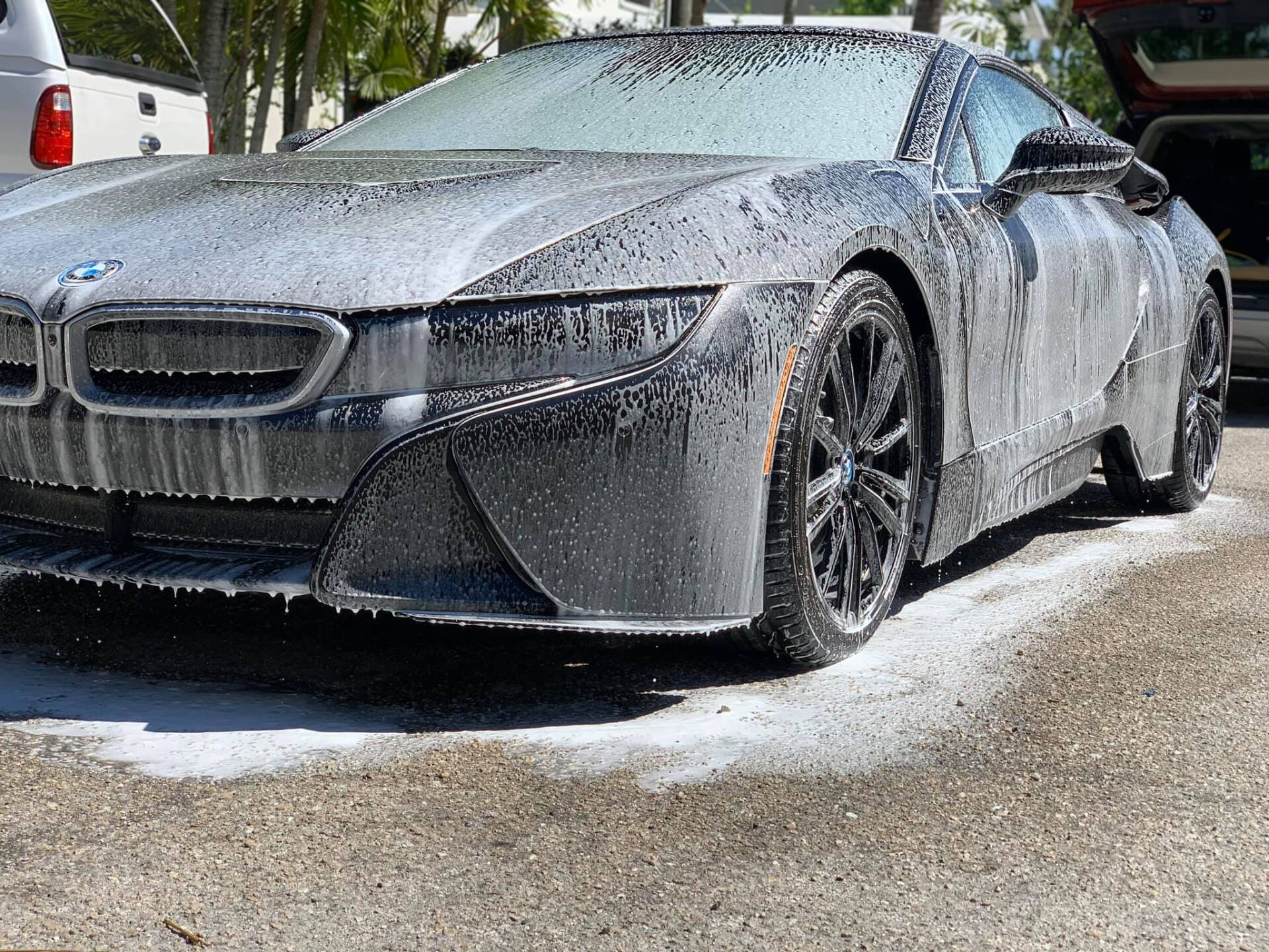 A silver BMW i8 covered in white soap suds, parked outside, being washed.