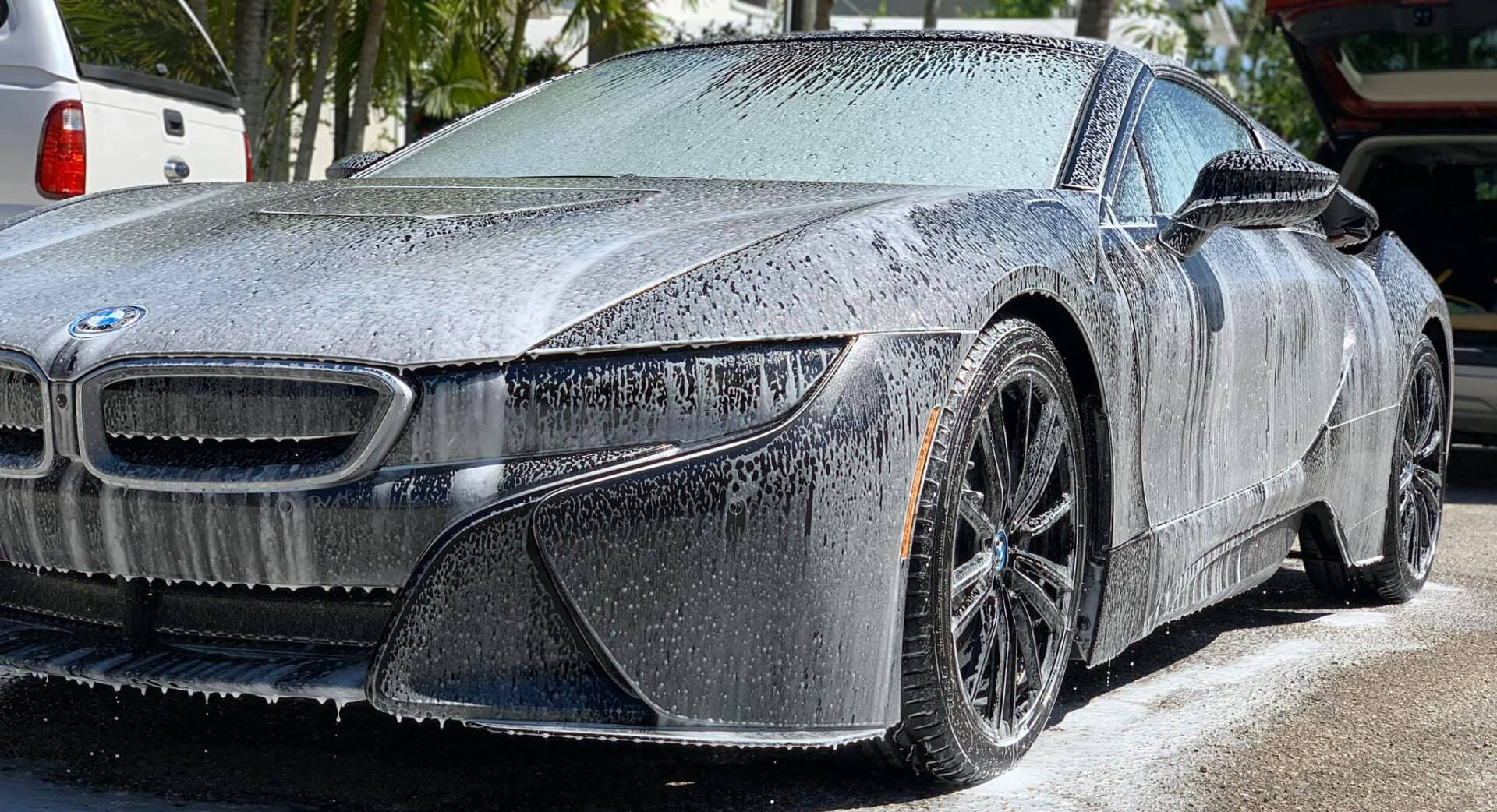 A gray BMW i8 covered in soapy foam during a car wash.