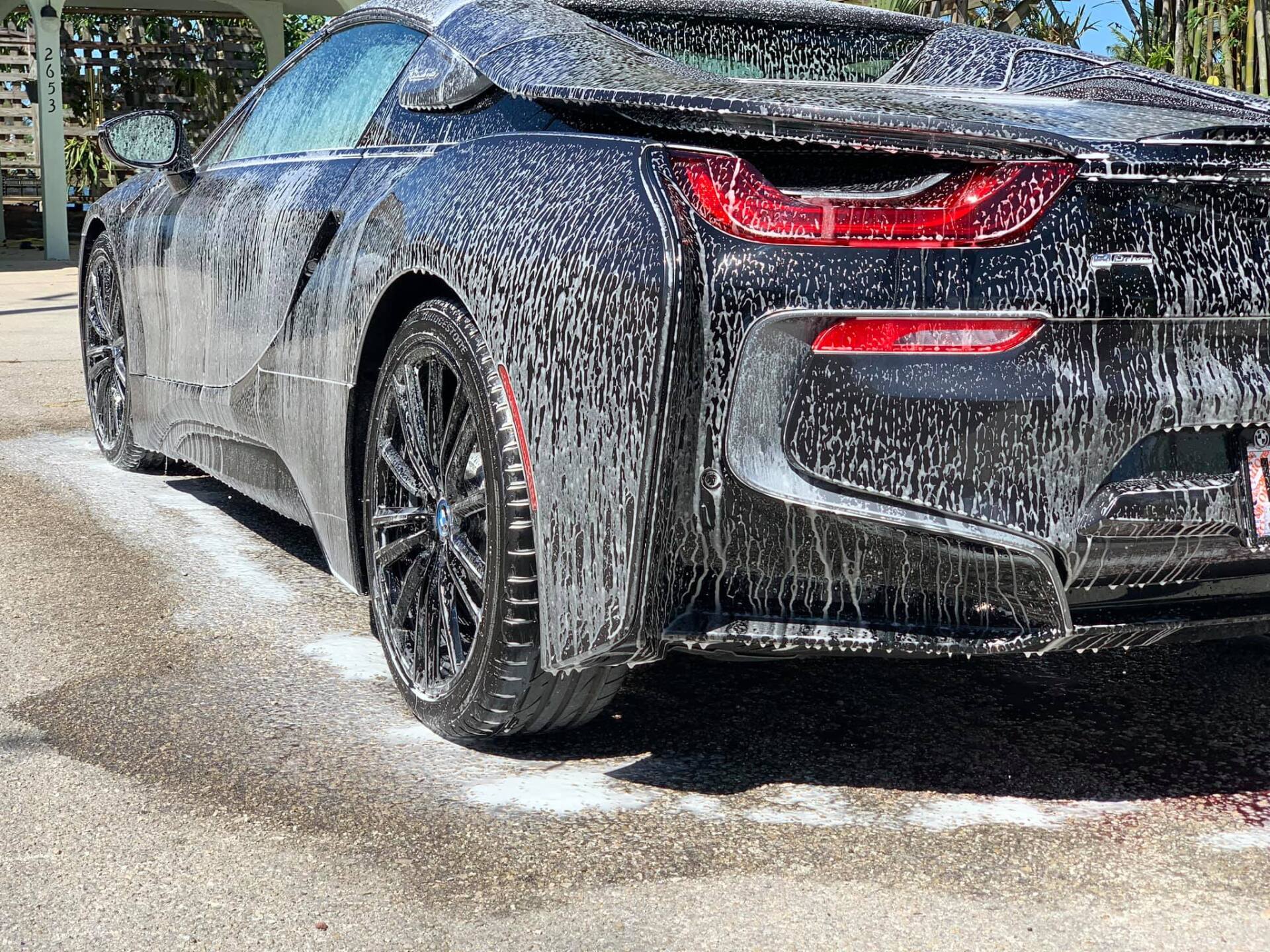 Black BMW i8 being washed with soapy foam outdoors.
