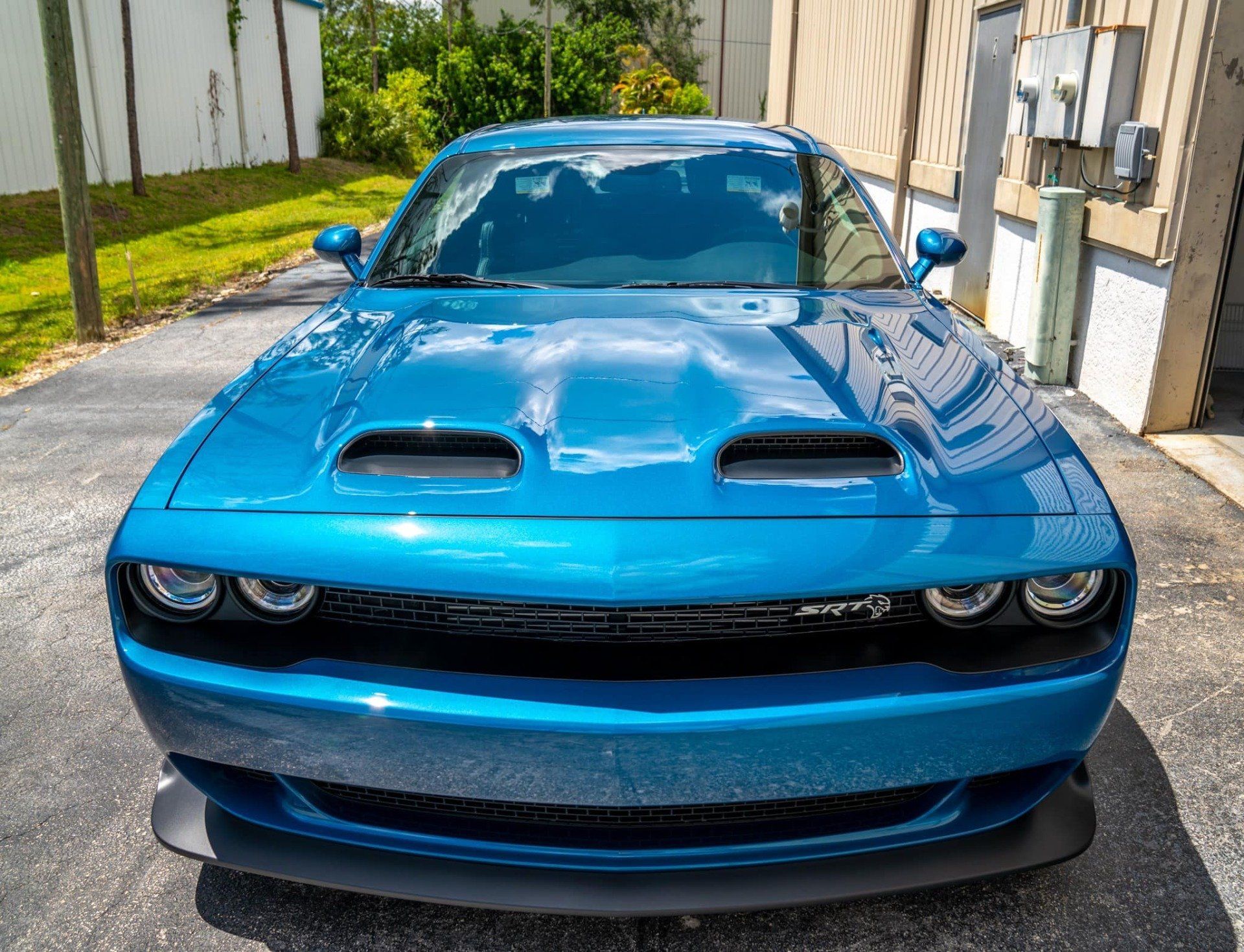 Blue Dodge Challenger parked, with hood scoops, in a driveway, sunny day.