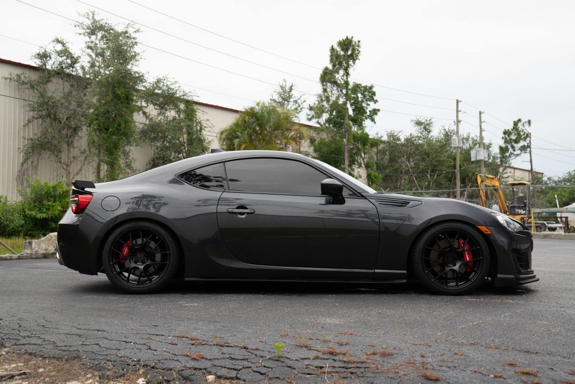 Dark grey sports car with black wheels and red brake calipers parked on asphalt.