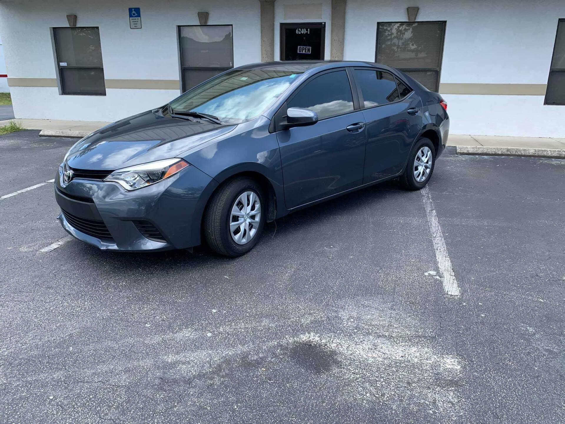 Dark blue Toyota Corolla parked in a lot in front of a building.