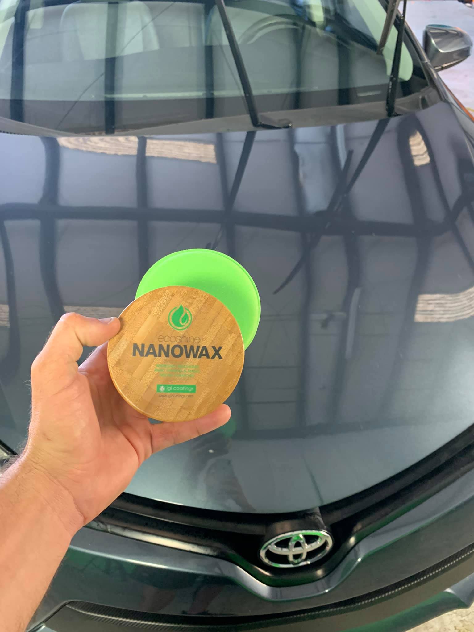 Hand holding Nanowax product next to green polishing pad on a dark car hood.