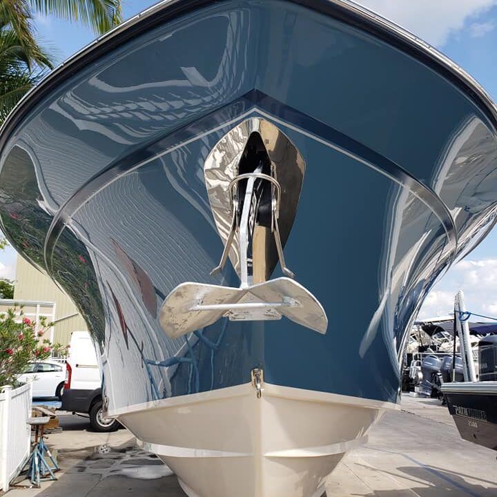 Blue and white boat with anchor at the front, parked outside on a sunny day.