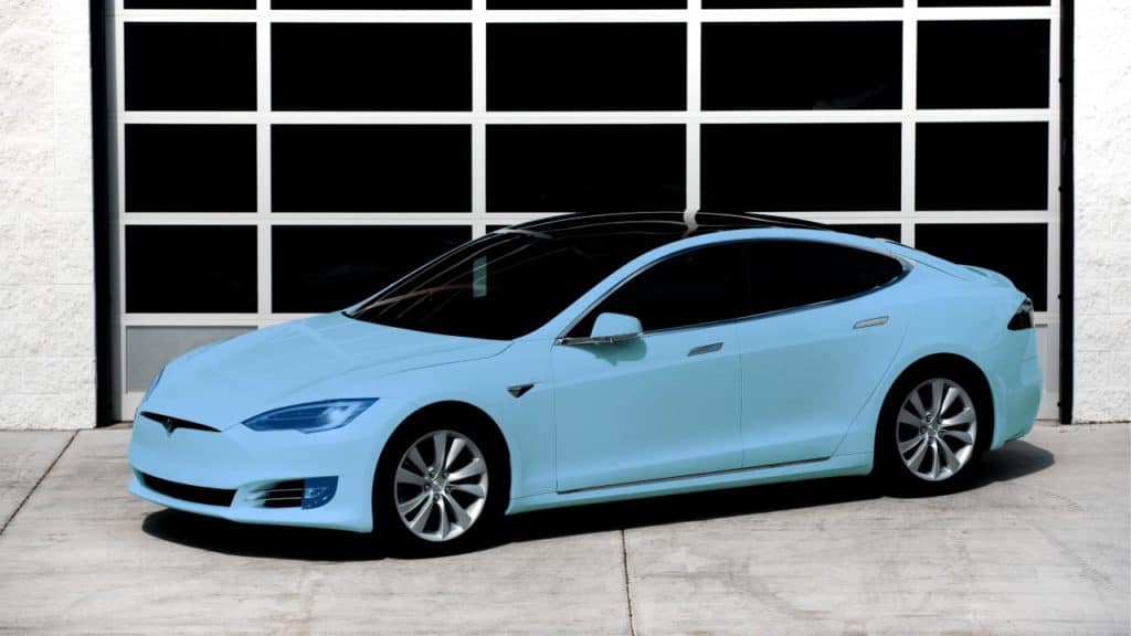 Light blue Tesla car parked in front of a building with a black and white garage door.