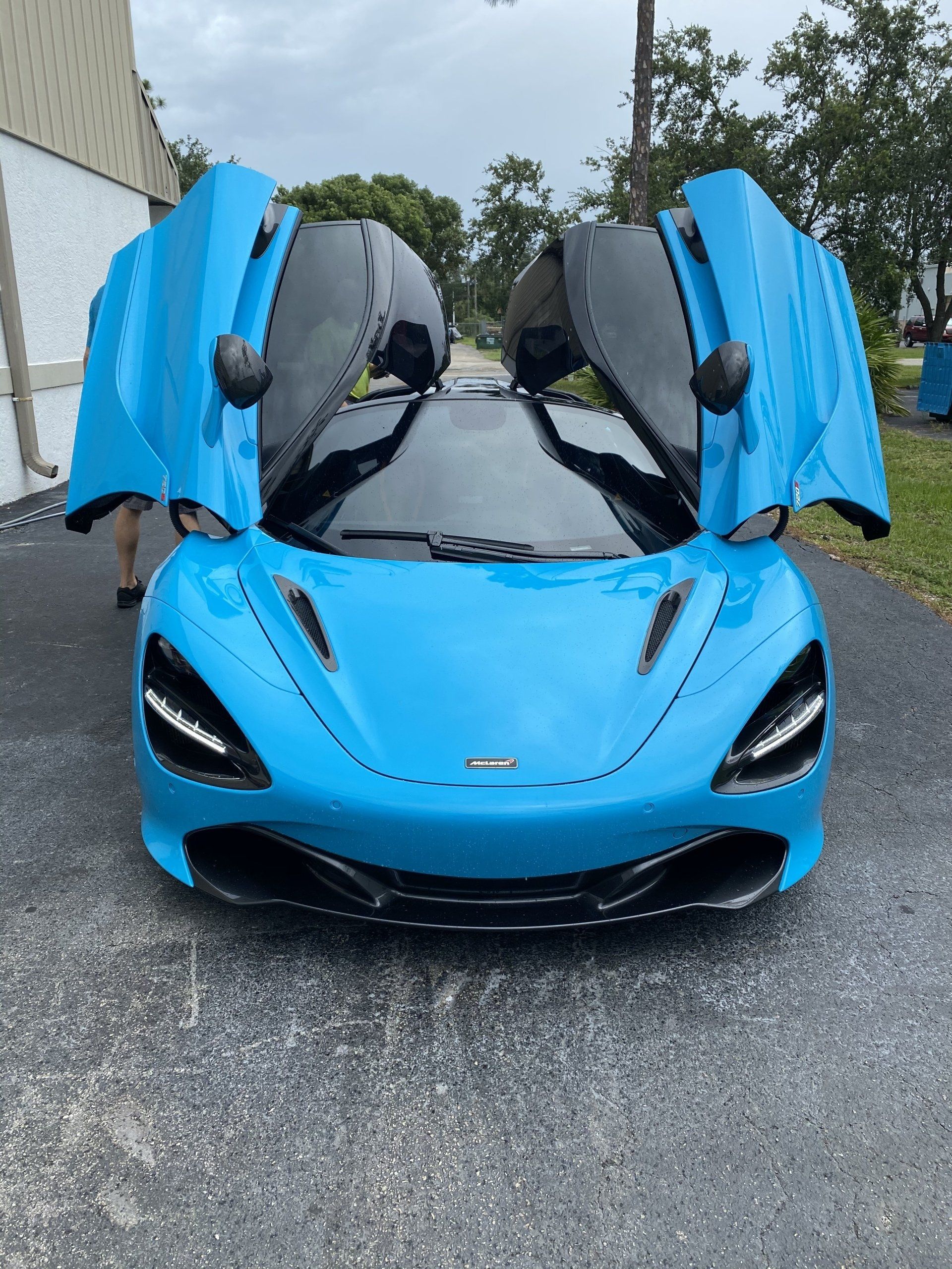 Blue McLaren sports car with doors open, parked on pavement.
