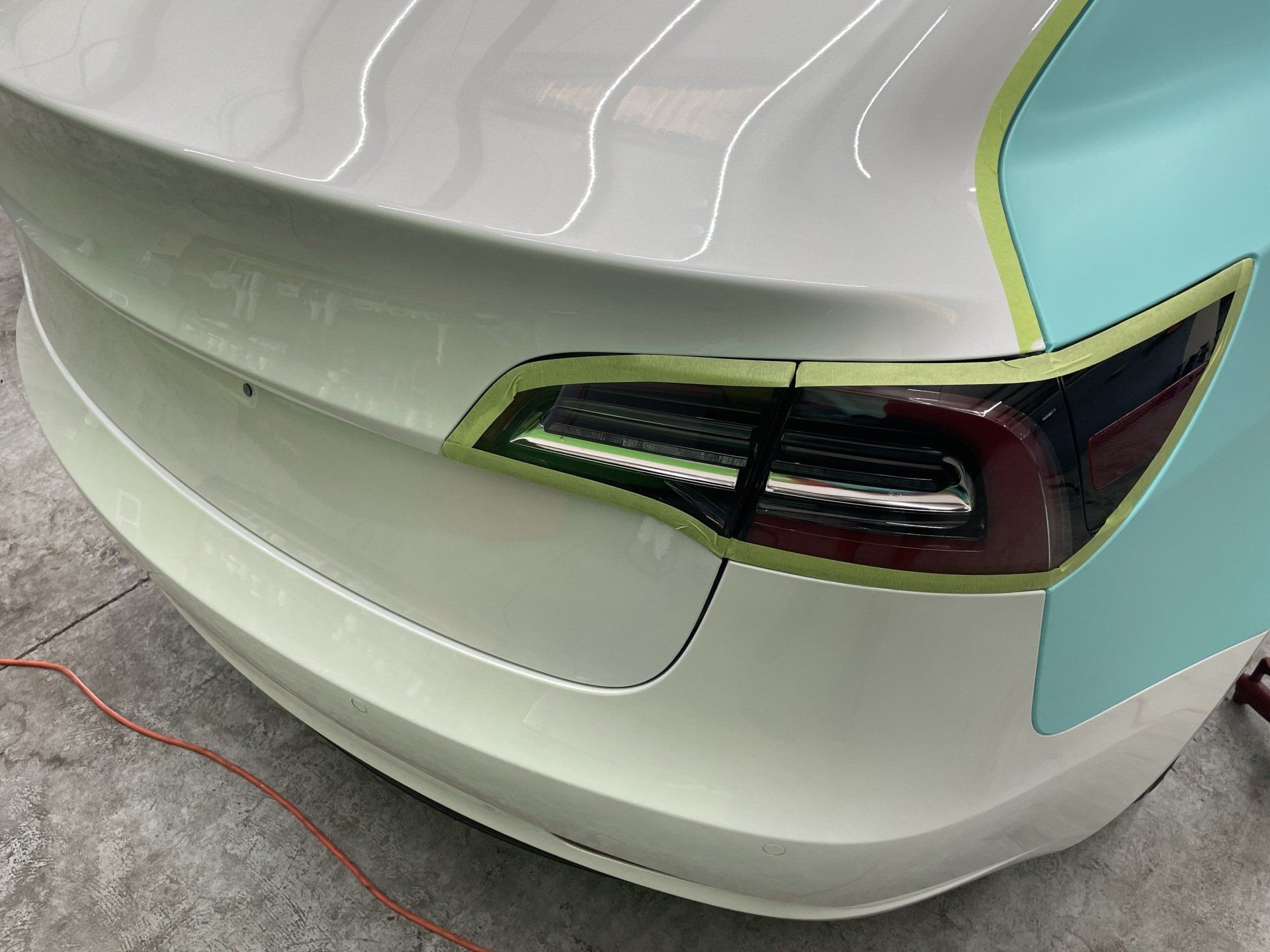 Rear of a white Tesla car masked with green tape, partially wrapped in teal.