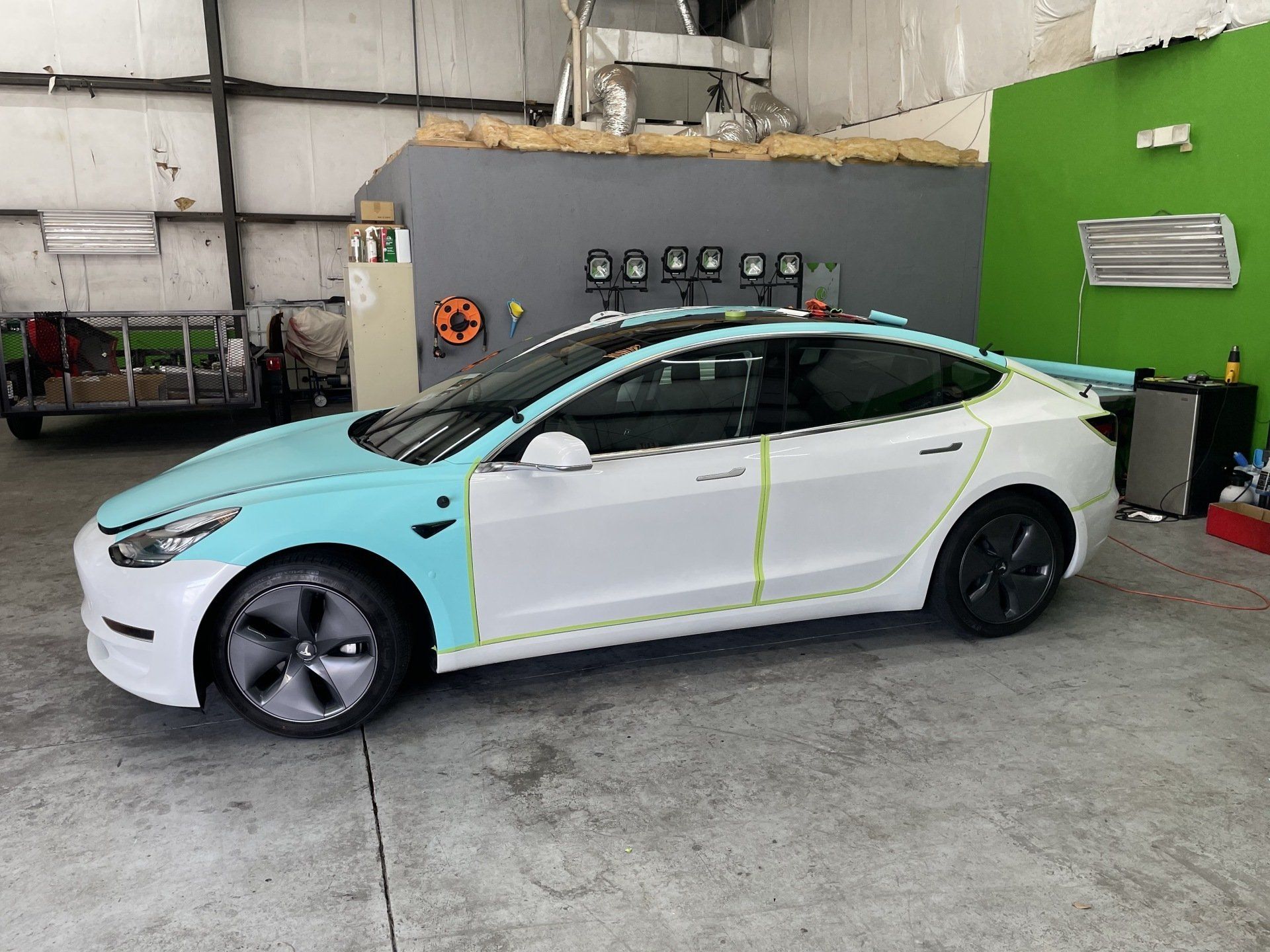 A partially wrapped white Tesla car with blue front panels, in a garage setting.
