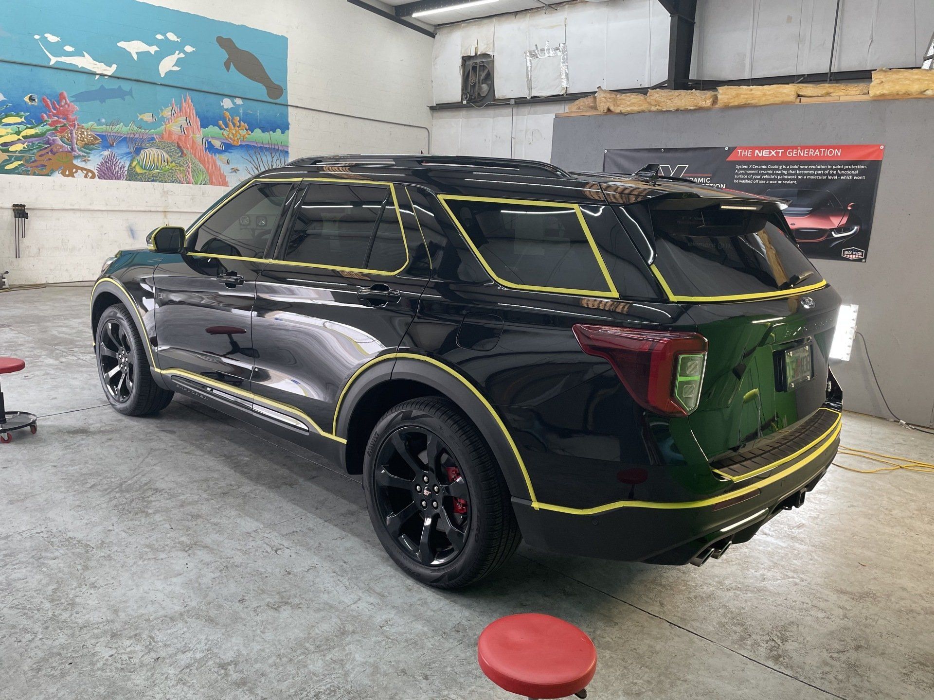 Black SUV with yellow tape in a garage, prepping for detailing.