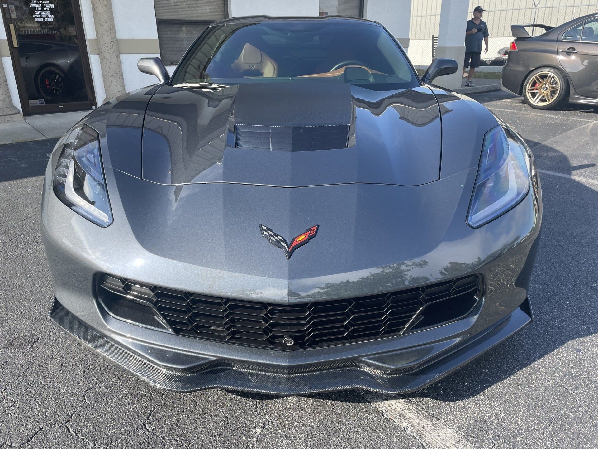 Gray Chevrolet Corvette with black hood and front spoiler, parked outside.