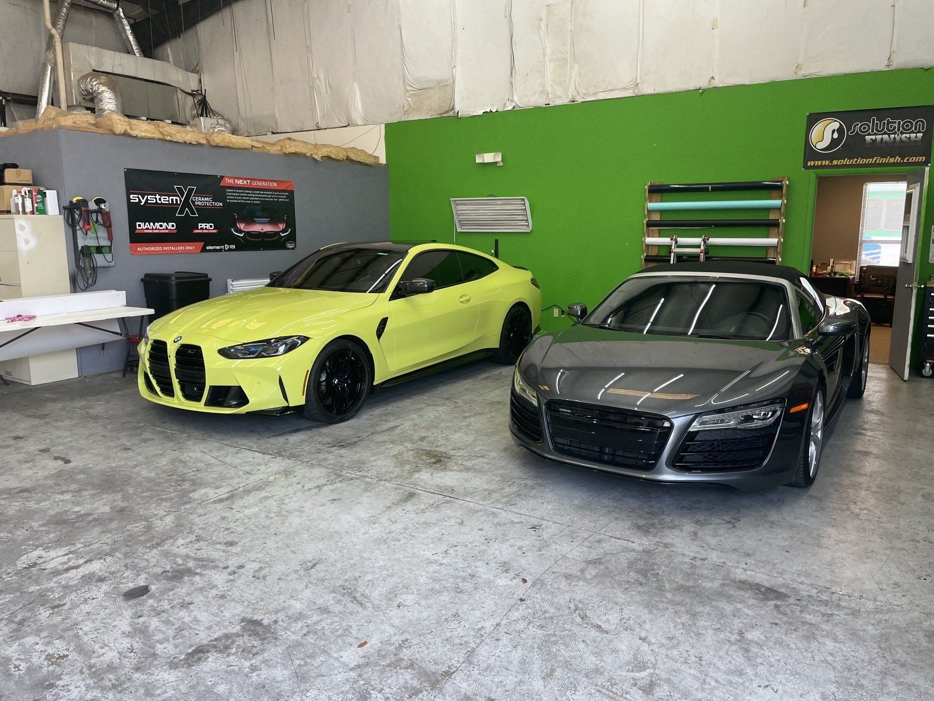 A yellow BMW M4 and gray Audi R8 inside a garage.