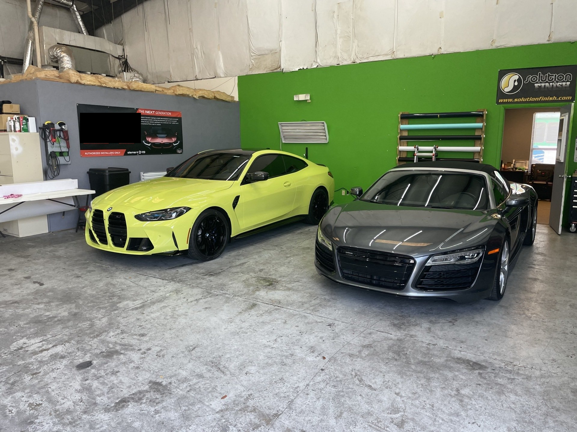 A yellow BMW and gray Audi in a garage. Green and gray walls.
