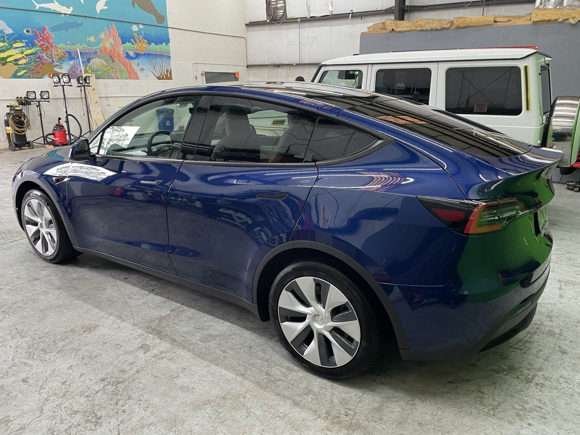 Blue Tesla Model Y parked in a garage, with a white SUV in the background.