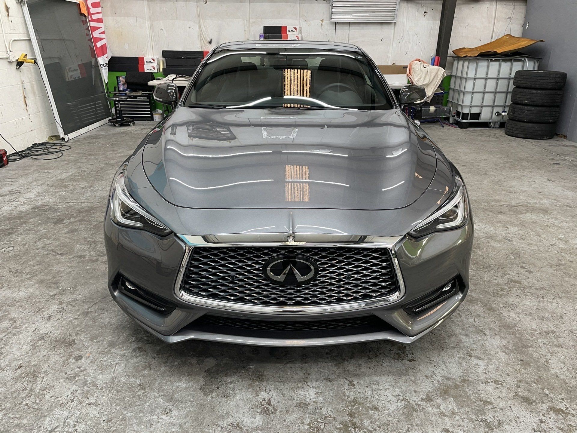 Gray Infiniti car in a garage, viewed from the front. Shows grille, headlights, and glossy surface.
