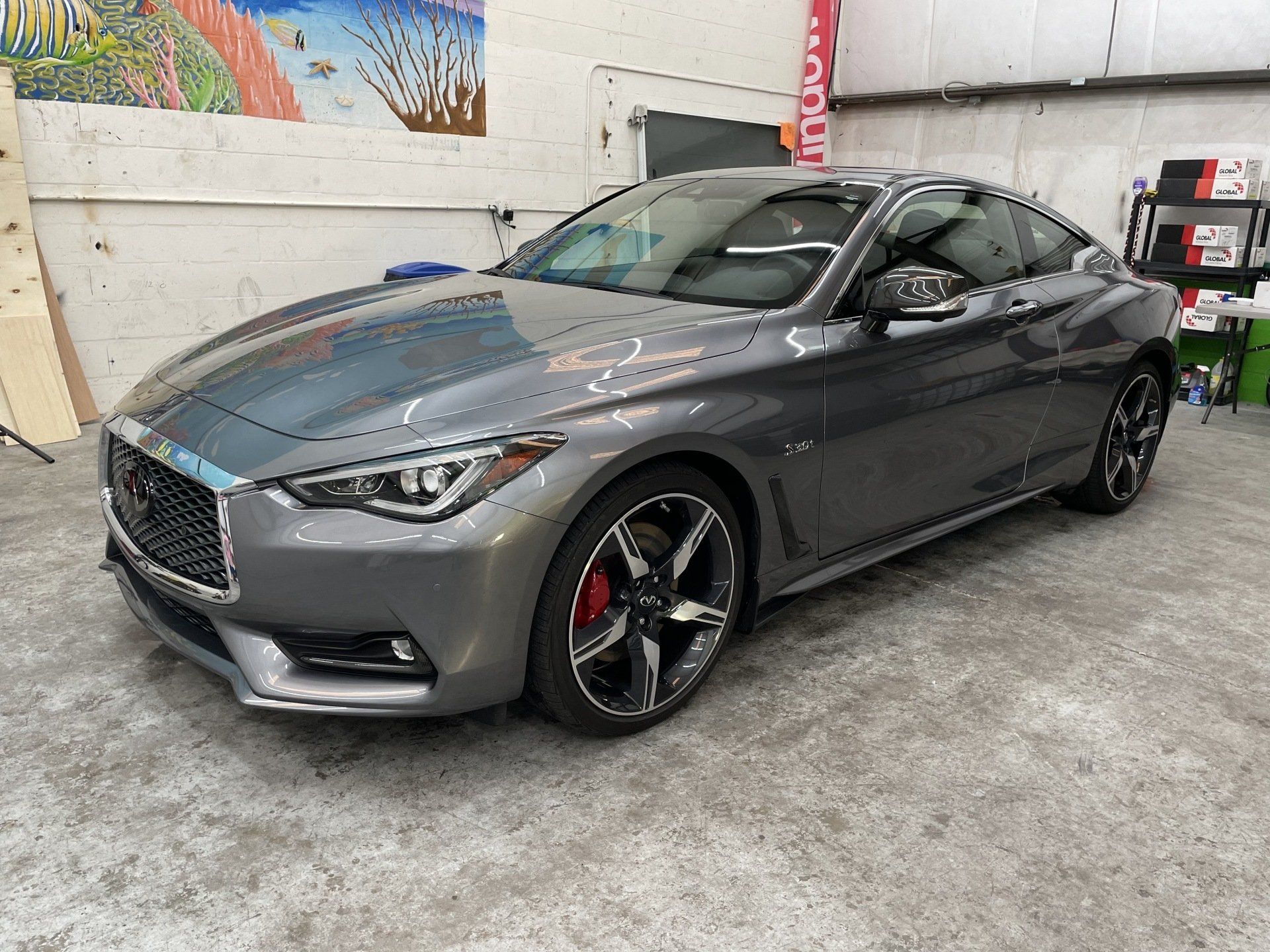 Gray Infiniti Q60 coupe parked in a garage with red brake calipers visible.