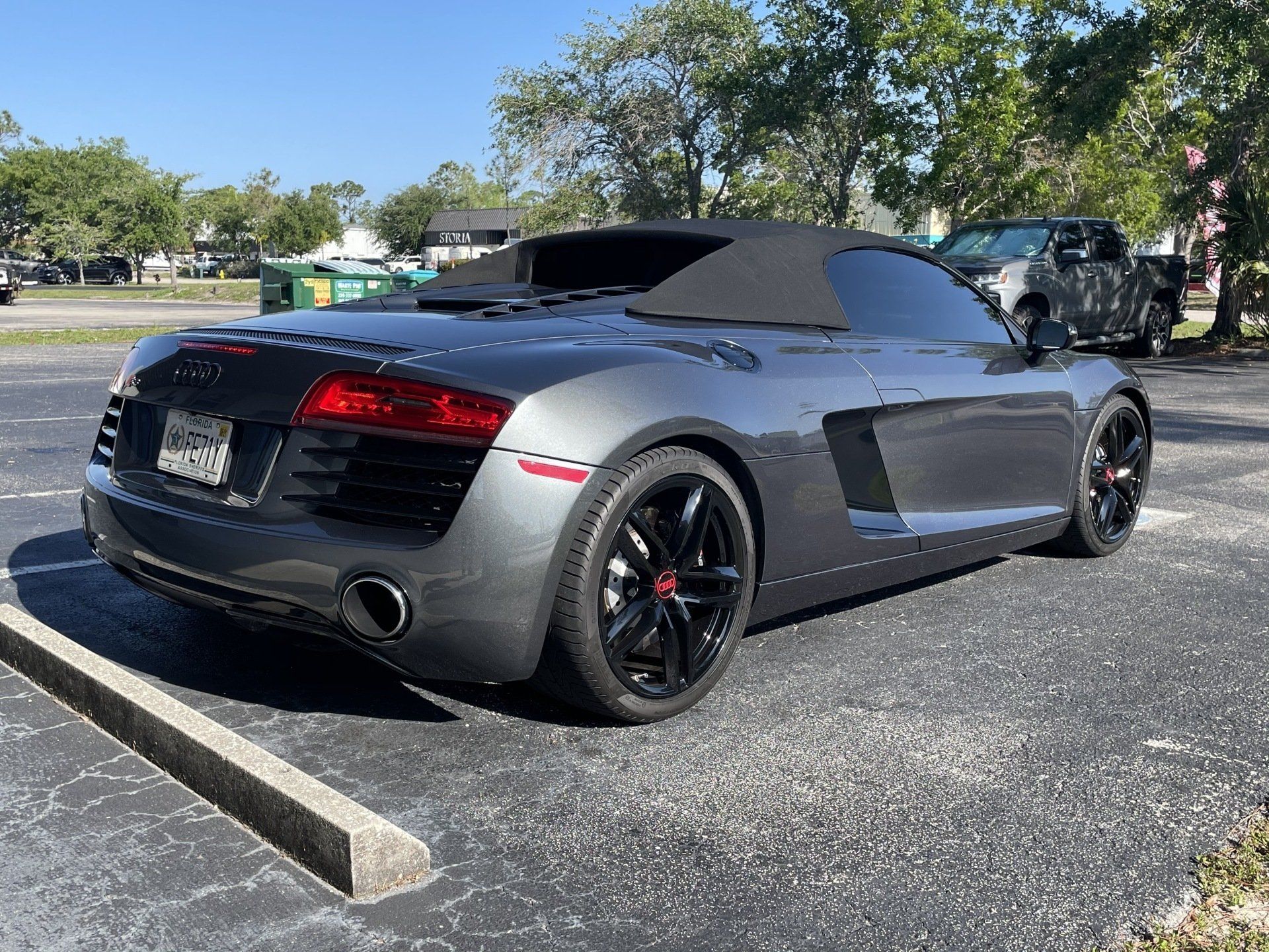 Gray Audi R8 Spyder convertible parked outside on a sunny day. Black wheels, red accents.