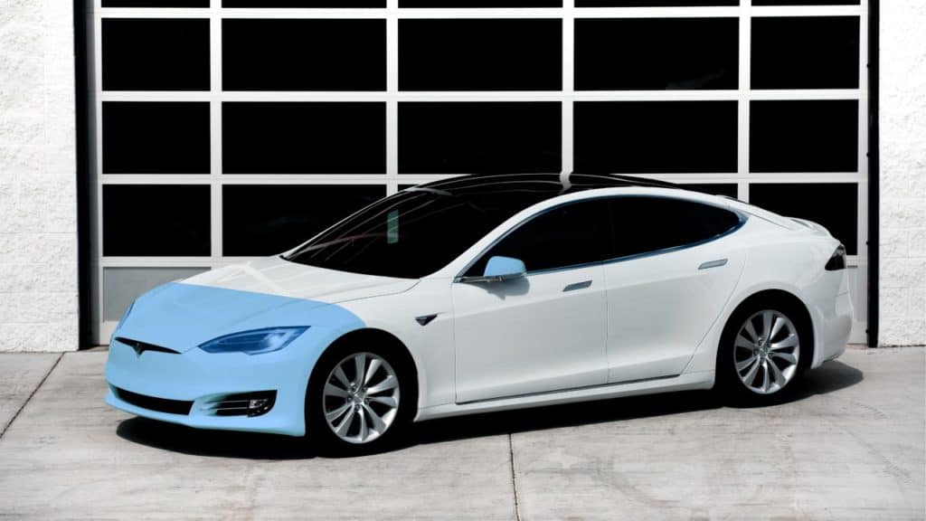 White Tesla car with blue front end parked in front of a garage.