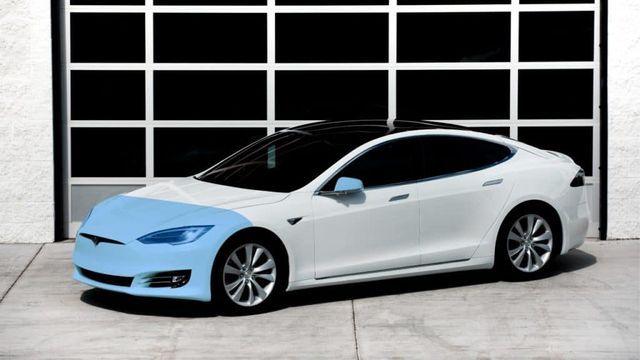 White Tesla car with blue highlighted front against a garage door.