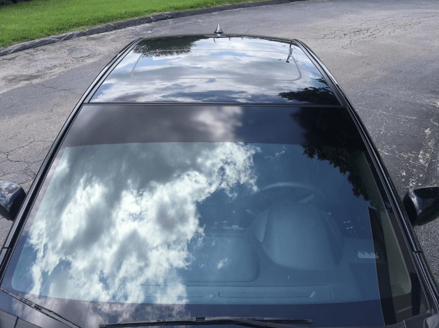 Overhead view of a black car's roof, reflecting the sky with clouds.