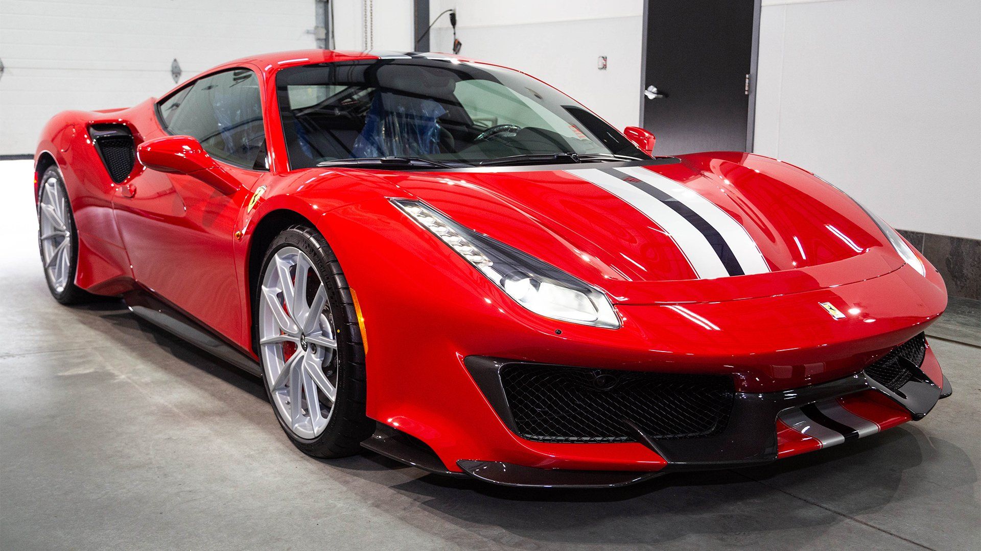 Red Ferrari sports car with white racing stripes in a garage.