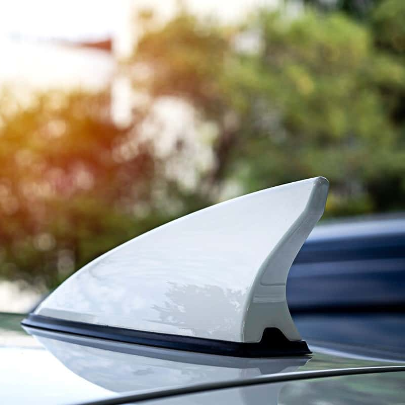 White shark fin antenna on top of a car, against a blurred background.