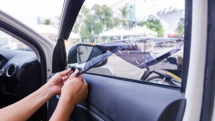 Person applying tint to a car window, using a tool to smooth it onto the glass.
