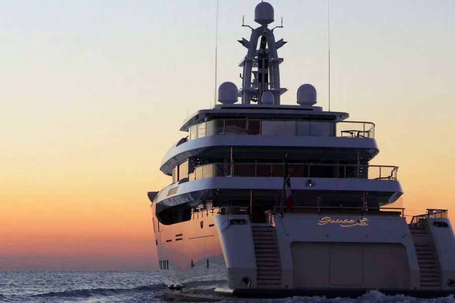 Luxury yacht cruising on water at sunset, orange and yellow sky.